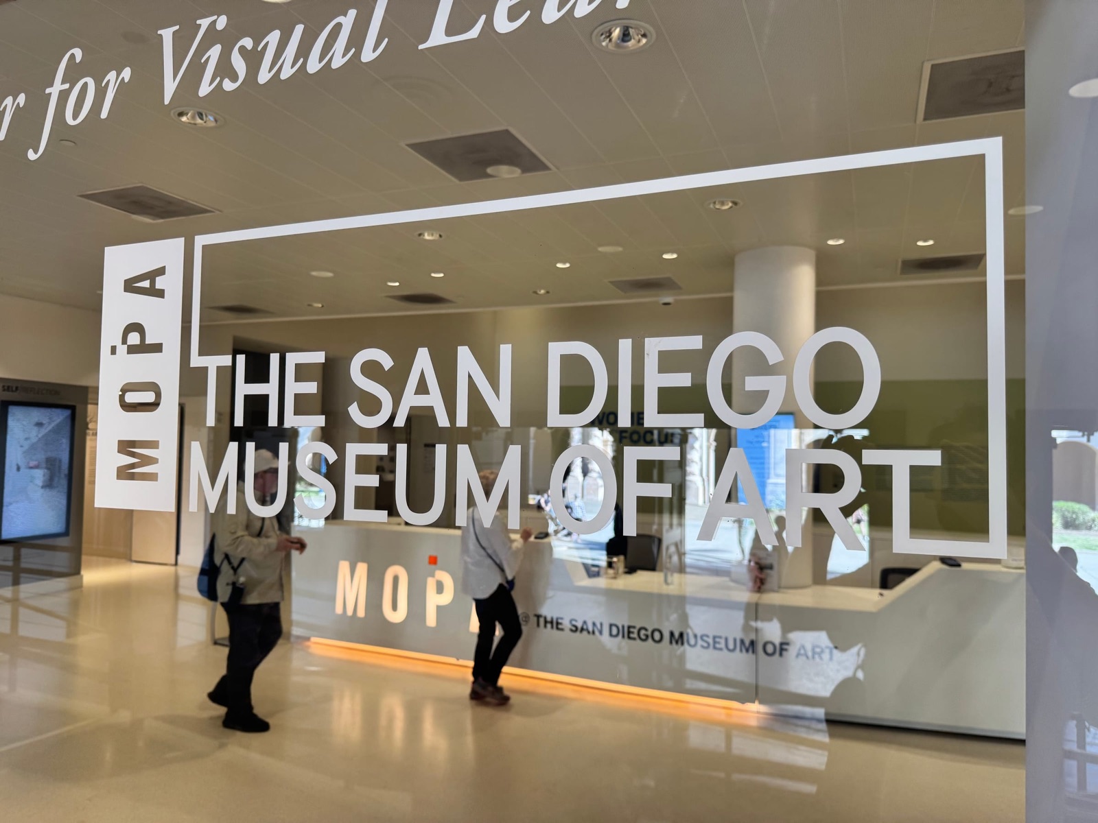 Glasfront des San Diego Museum of Art mit großem Schriftzug, dahinter zwei Personen im Foyer.